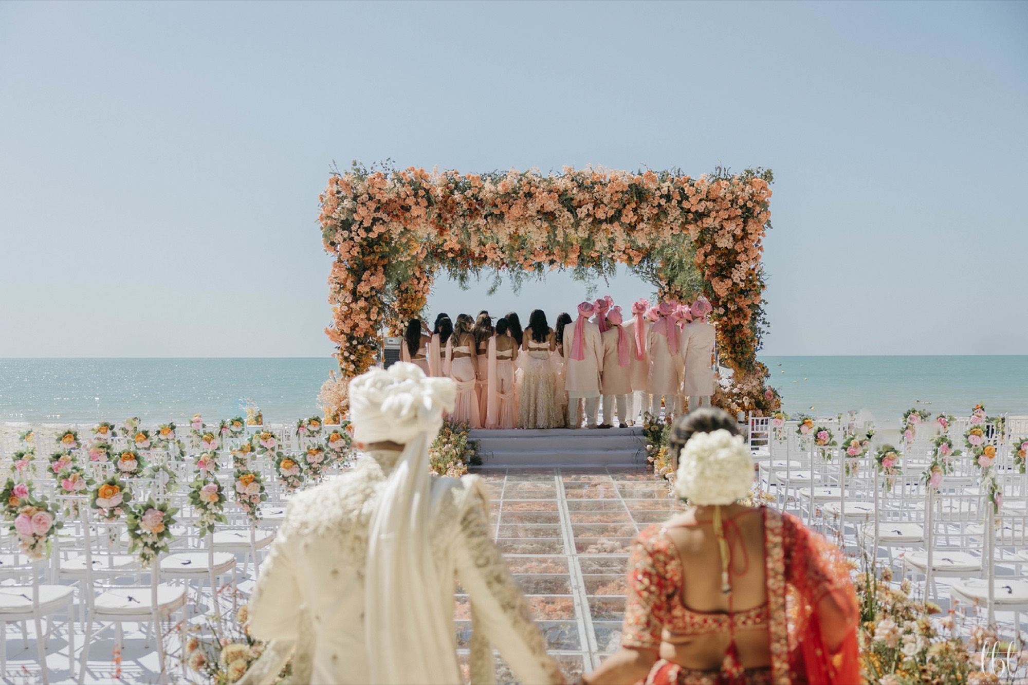 Looking down a beach aisle toward the floral mandap and ocean